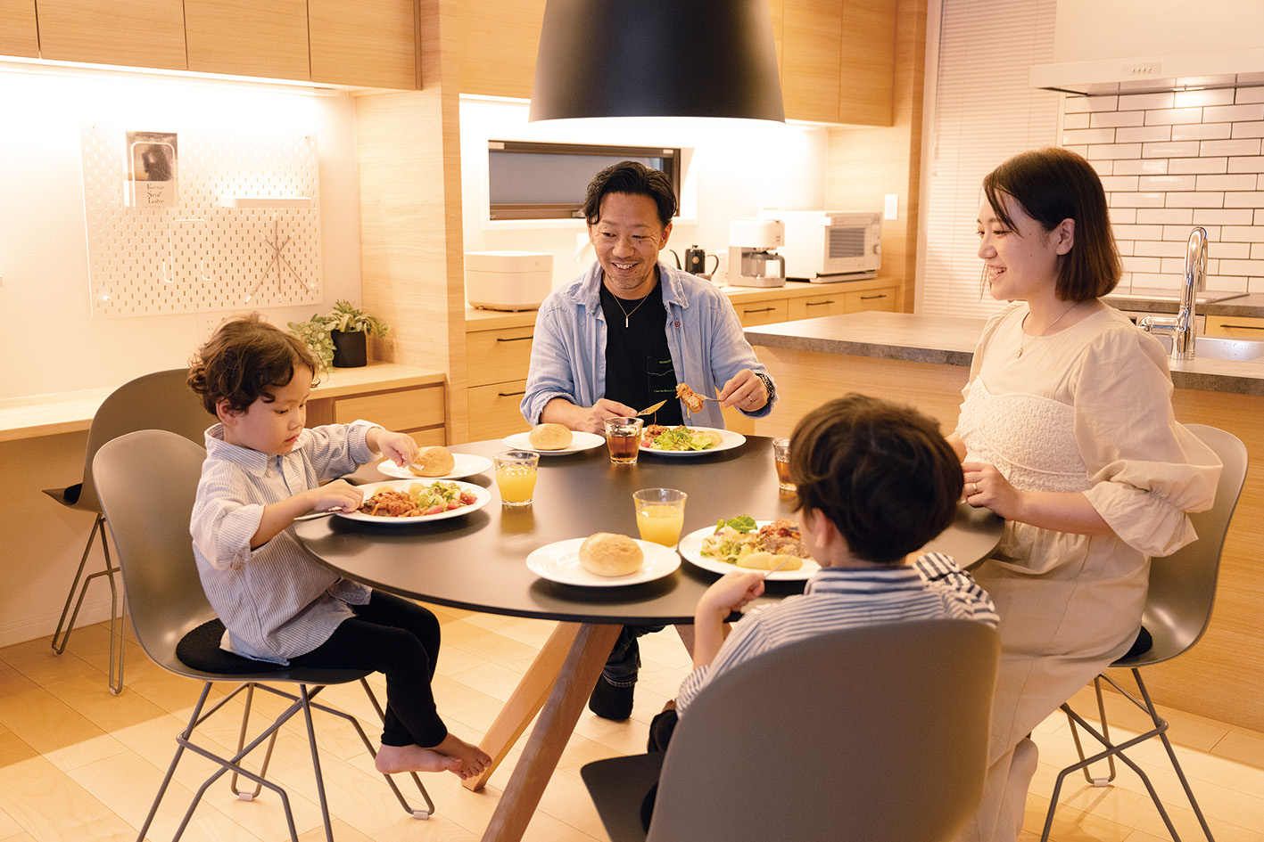 明るい木目調のダイニングで丸いテーブルを囲み食事を楽しむ父・母・男の子2人の4人家族